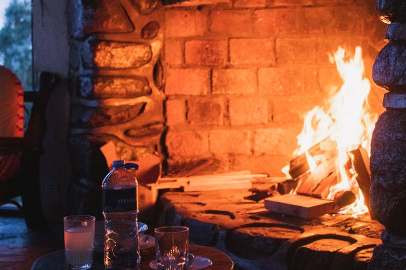 The stone fireplace lit in the evening, with drinks on a low table in front
