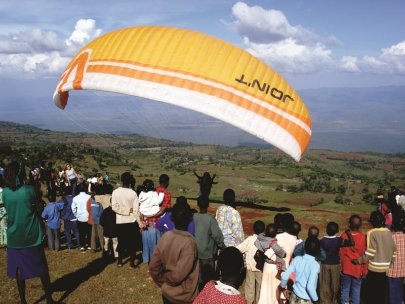 A paraglider coming in to land beside the lodge, watched by a crowd