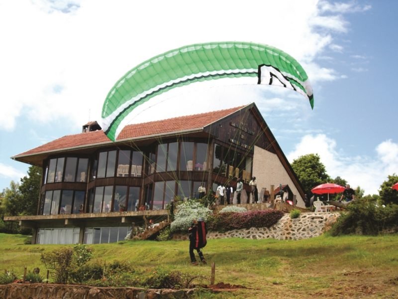 A paraglider passing directly over the lodge building